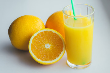 Glass with orange juice next to orange slices on a white background.