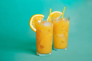 Glasses of orange juice with ice on a green background