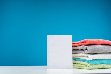 Close up of white board with pack of washing powder isolated on blue background. Pile of folded...