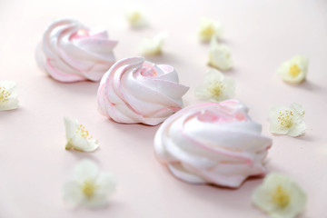 Fototapeta na wymiar White homemade meringue or marshmallow on pink background with small white flowers