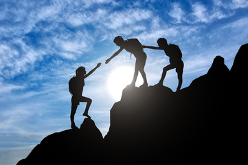 Silhouette of two female mountaineers helping another female mountaineer to overcome the obstacle...