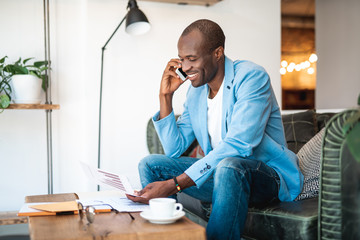 Portrait of beaming businessman telling by mobile while working with graphics. He sitting on sofa