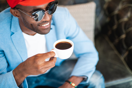 Laughing man tasting mug of appetizing beverage while relaxing indoor. Satisfied employer during rest concept