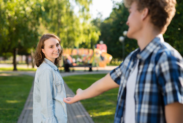 In the summer in park in nature. The young man gets acquainted with the girl. She stretches out her hand for communication. The girl smiles happily says yes. Dating in the city.