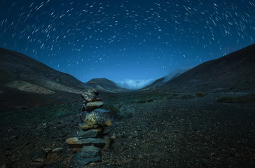 Star Trails in dürrer Steppe mit gestapelten Steinen
