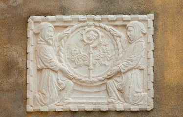 Religious symbols in Venice. Crosier staff between two hooded monks, an ancient stone relief on a wall in the historic center