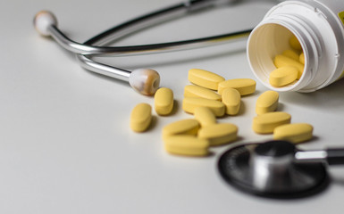 Multicolored pills and capsules on white background, phonendoscope