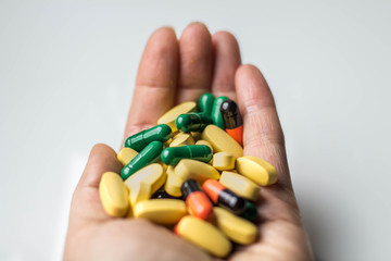 Multicolored capsules and pills in hand, white background