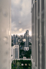 Rain over Bangkok: Out of focus cityscape behind the window glass with rain drops.