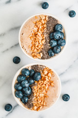 Top view of smoothie bowls with fresh ripe blueberry, nuts, chia, banana and soya milk over white background. The concept of healthy eating and vegetarian food.