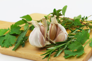 Closeup of garlic cloves and bunch of fresh herbs on wooden board
