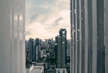 Rain over Bangkok: Out of focus cityscape behind the window glass with rain drops.