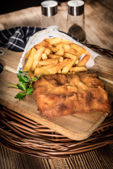 A piece of fried cod with fries on cutting board.