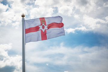 Flag of Northern Ireland in the sky/ Flag of Northern Ireland in the wind on a flagpole against a background of clouds in the sky