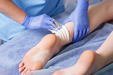 Hands doctor cosmetic smear sugar paste next to the heel of the left foot to a young woman