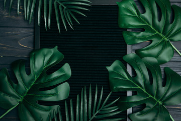 Fototapeta premium top view, tropical leaves and board with copyspace on a dark background