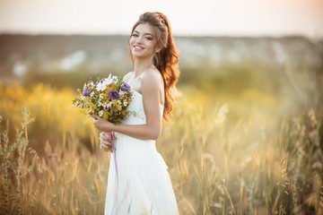 Fototapeta na wymiar Beautiful young bride with fashion bouquet of wildflowers in field over sunset lights