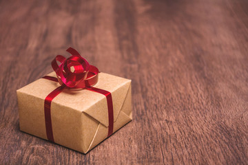 A gift, tied with a red ribbon and wrapped in kraft paper on a wooden background.