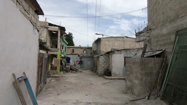 The gray shabby walls of the squalid buildings of the slums of the Dominican Republic. Walk along the narrow street of the poor area of Santo Domingo. Extreme tourism through the slums.