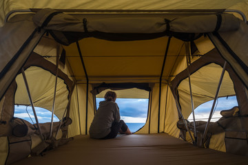 lonely independent strong middle age woman feeling the nature outdoor in a roof tent on the car. travel and lifestyle wanderlust concept for beautiful caucasian lady sitting in front of the ocean © simona