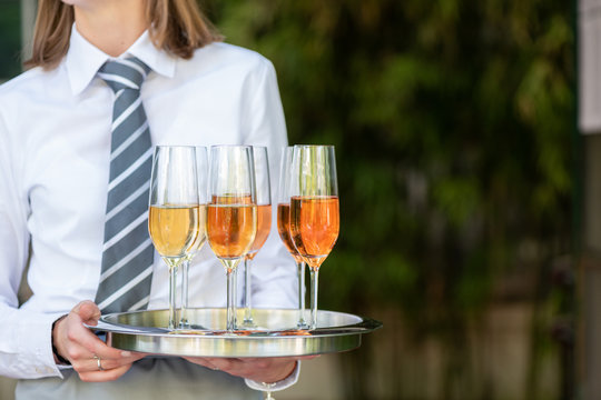 Junge Kellnerin mit wei&szlig;em Hemd und Krawatte h&auml;lt ein silbernes Tablett mit Champagner Gl&auml;sern in der Hand