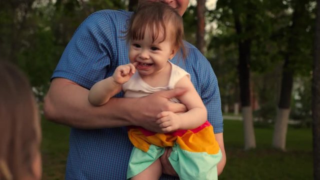 Baby laughs at hands of loving father. Baby and dad laugh, playing together for a walk in park. Dad throws child in air on street for fun.