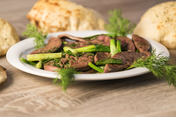 lamb liver food with green vegetables in the plate and local bread on the wooden table for restaurant and kitchen concept.