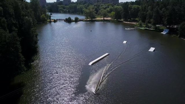 Aerial shot of a cableway in a lake with a wakeboarder grinding and rotating on a funbox