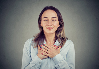Faithful woman with eyes closed keeps hands on chest near heart, shows kindness