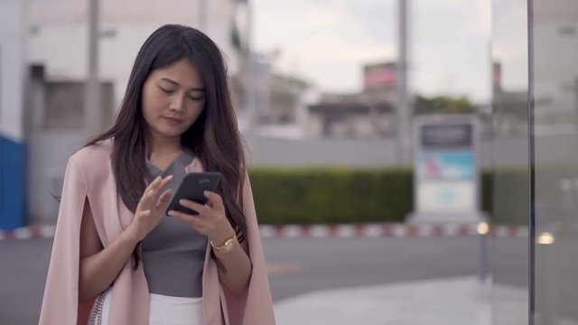 Asian women stand mobile phones in front of the mall.