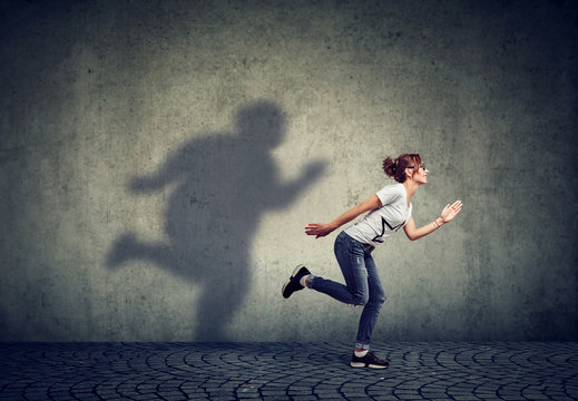 Woman running away from her fat shadow on the wall