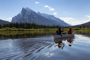 Couple adventurous friends are canoeing in a lake surrounded by the Canadian Mountains. Taken in...