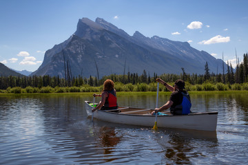 Couple adventurous friends are canoeing in a lake surrounded by the Canadian mountains. Taken in Vermilion Lakes, Banff, Alberta, Canada.