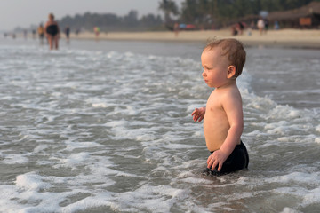 A little boy walks into the sea at sunset on his own