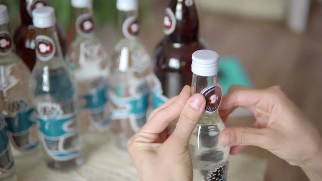 Close-up of a girl glues stickers on glass bottles with homemade alcohol