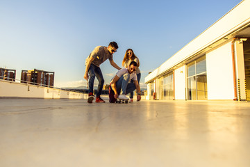 Young cheerful friends playing and driving skateboard on the rooftop. Young and careless friends...