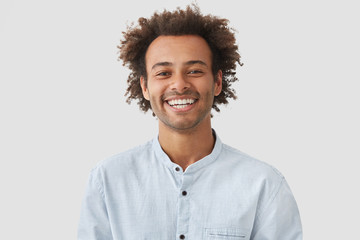 Happy mixed race male student with Afro hairdo shows white teeth, being in good mood after classes...