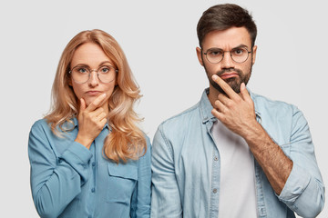Horizontal shot of thoughtful male and female colleagues hold chins and being concentrated on...