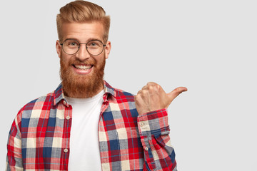 Happy positive male with long thick ginger beard and mustache, has friendly smile, dressed in...