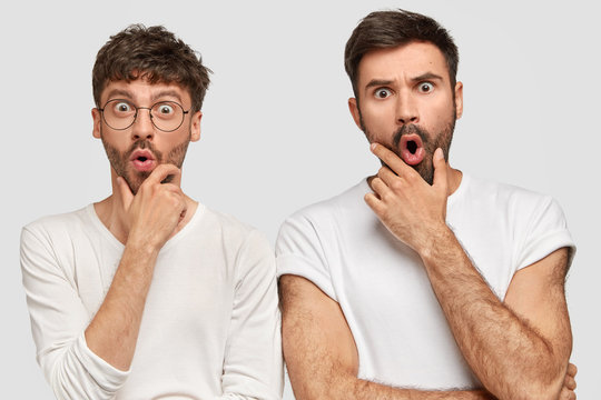 Suprised Male Corporate Workers Have Stunned Expressions, Hold Chins And Stare With Bugged Eyes, Shocked To Recieve Failure, Dressed In Casual White T Shirts, Pose In Studio. Team Work Concept