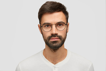 Close up portrait of handsome unshaven male with thick beard and mustache, has dark hair, looks...