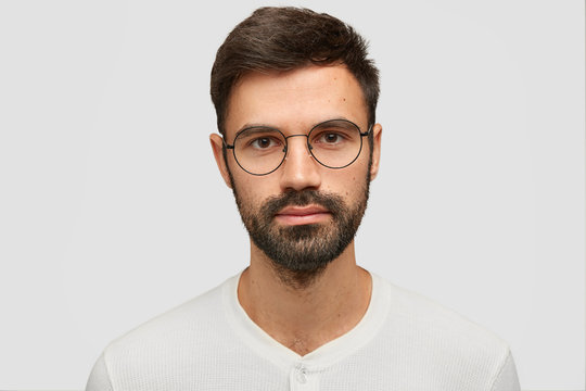 Close up portrait of handsome unshaven male with thick beard and mustache, has dark hair, looks seriously at camera, thinks about something, isolated over white background. Facial expressions concept