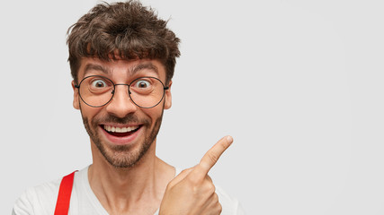 Positive funny young guy with gentle toothy smile, being in high spirit, rejoices as sees something...