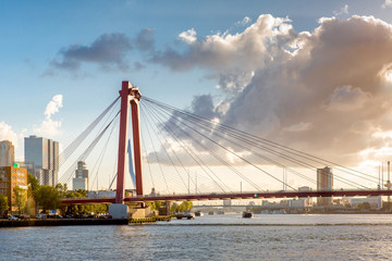 Fototapeta na wymiar Sunset cityscape of Rotterdam with a highway bridge in the foreground, and downtown and the famous Erasmus bridge in the background against a blue sky