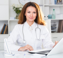 Portrait of woman in uniform who is working behind laptop with documents