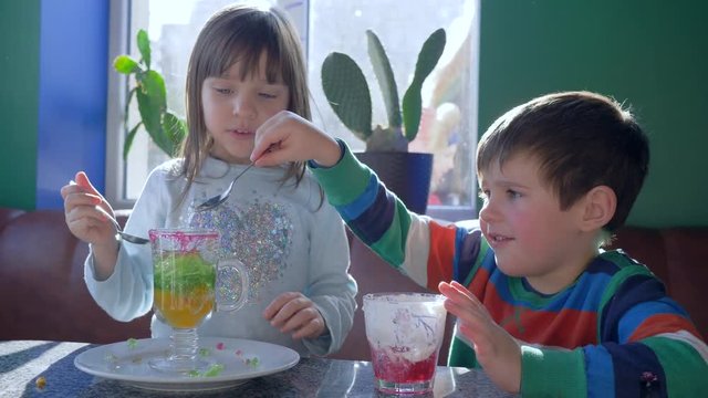 dessert time, cheerful friends eat pudding from glass of each other sitting at table in cafe