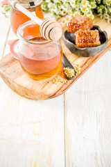 Organic floral honey, in jars, with pollen and honey combs, on a white wooden table, with wildflowers, copy space