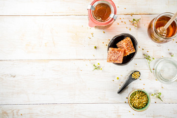Organic floral honey, in jars, with pollen and honey combs, on a white wooden table, with...