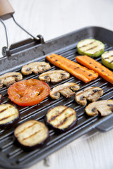 Grilled vegetables in a grilling pan on a white wooden background, side view. Close-up.
