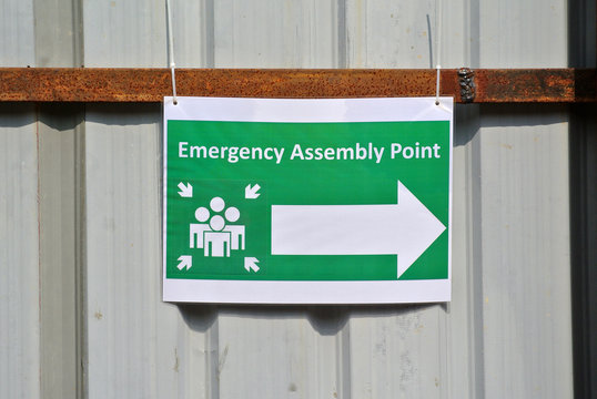 Safety signage "Emergency Assembly Point" with direction arrow at the construction site. It used to make sure workers know where to gather during emergency. 